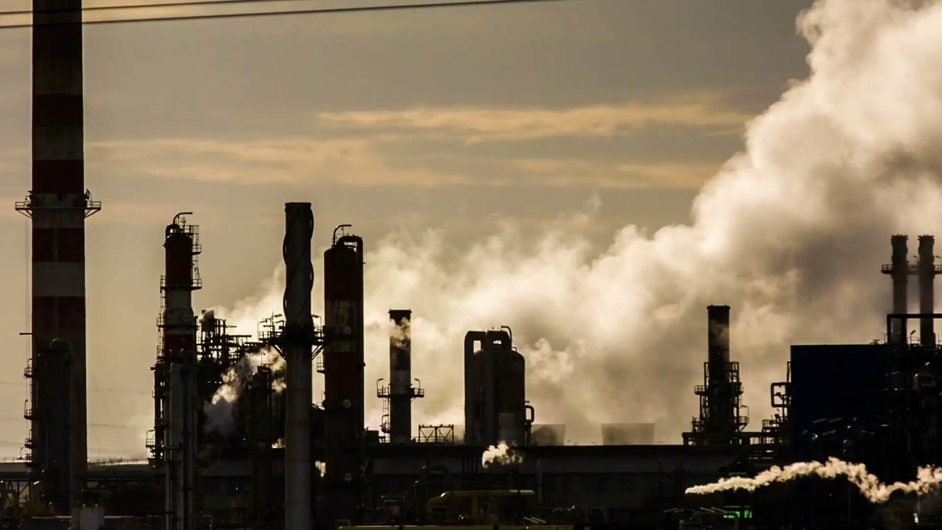 Industrial smokestacks in silhouette with clouds of smoke and steam rolling into a hazy sky