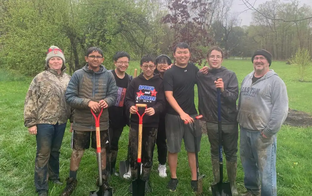 Students and volunteers with muddy shovels and boots at the end of a rainy planting day